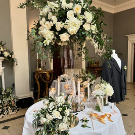 Elegant wedding display with tall bouquet of white flowers, greenery, candles on a round table