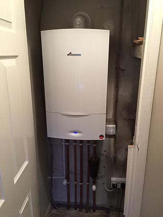 A white boiler unit is mounted on a wall in a narrow utility space