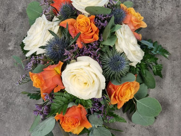 A bouquet with vibrant orange and white roses, accented by purple thistles and greenery