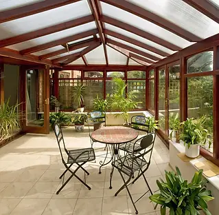 A sunlit conservatory features a round table with four metal chairs