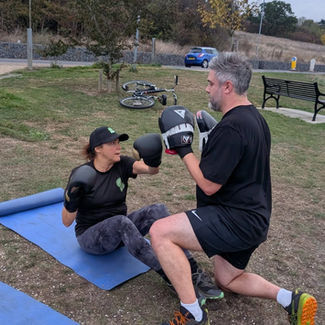 A woman wearing a cap and boxing gloves sits on a yoga mat