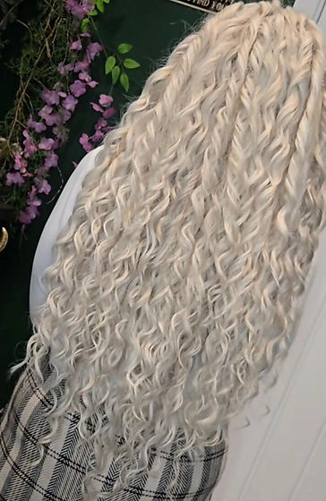 A person with long, curly, platinum blonde hair standing with their back turned.