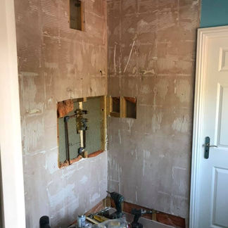 Partially demolished wall reveals plumbing pipes and insulation beneath removed tiles