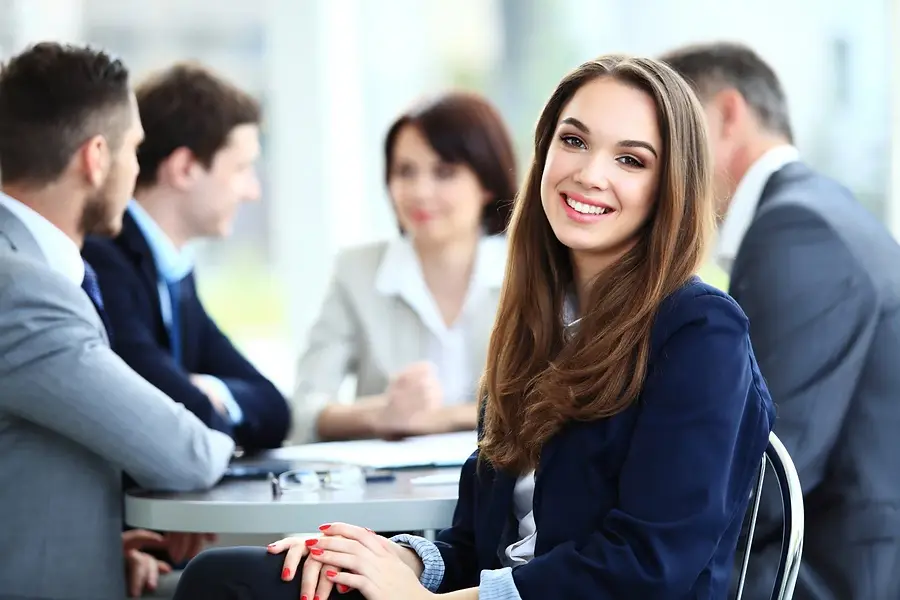 Smiling woman in a blue blazer sits at a table during a business meeting with four people 