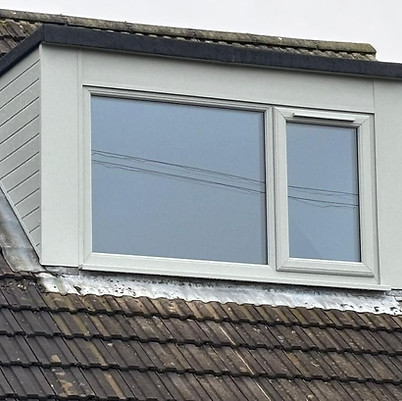 A dormer window with a white frame and two glass panes sits atop a roof with brown tiles