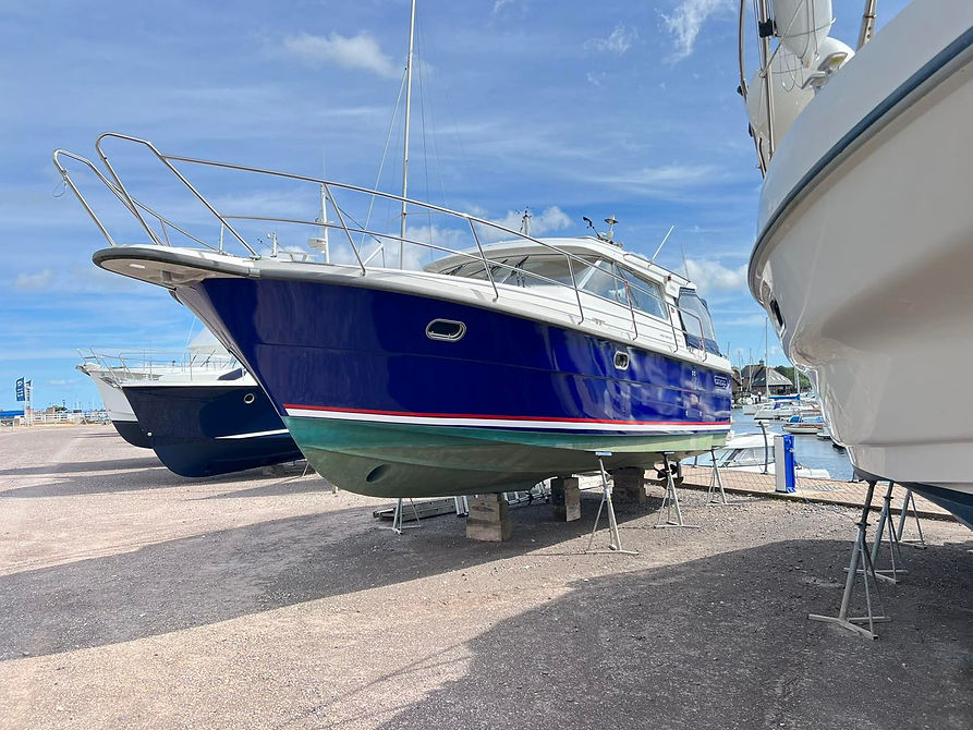A blue and white boat on stands at a marina under a clear sky, with other boats nearby