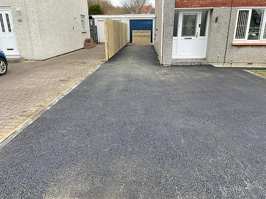 Freshly surfaced black tarmac driveway running down the side of a residential house towards a garage