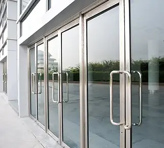 Glass sliding doors with silver frames and handles, reflecting a nearby building and greenery