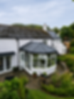 A quaint white cottage with a dark slate roof features a glass conservatory extension