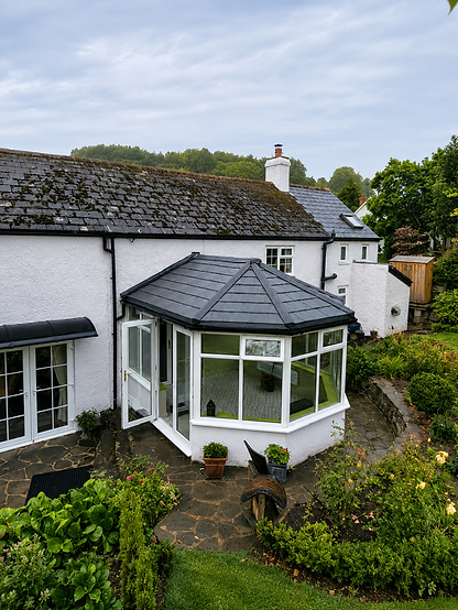 A quaint white cottage with a dark slate roof features a glass conservatory extension