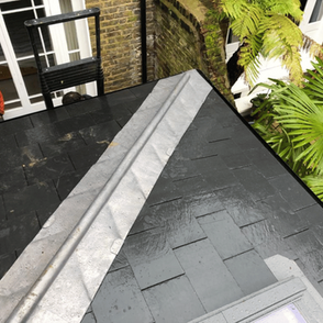 Wet roof with dark shingles, a central metal ridge, and a skylight