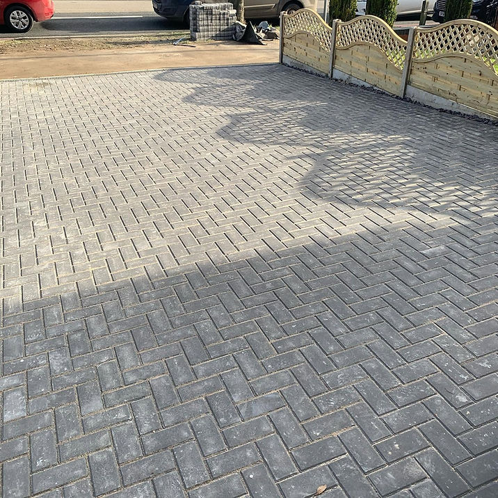 A close-up view of a grey block-paved driveway laid in a herringbone pattern