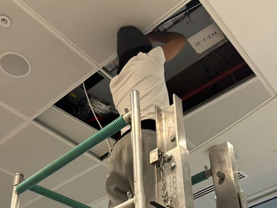 A worker on a scaffold accesses a ceiling panel