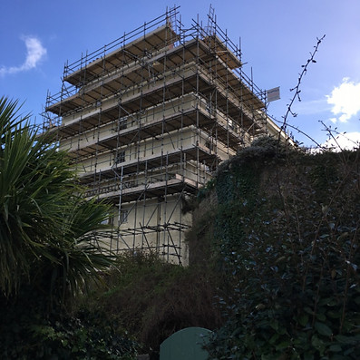 A nine-story building under repair, covered in scaffolding, with a clear blue sky.