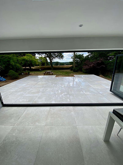 Large outdoor porcelain patio viewed through open black bi-fold doors looking out onto a garden lawn