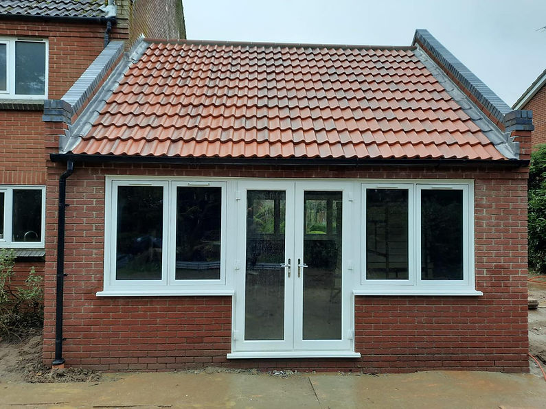 A small brick extension with a red-tiled roof features three white-framed windows