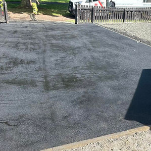 Large newly surfaced black tarmac driveway area next to a residential property
