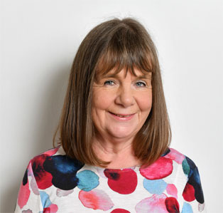 Smiling children´s book author Julia Donaldson n with shoulder-length brown hair, wearing a colorful floral top against a white background