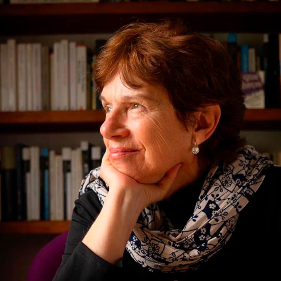 Smiling Author Yolanda Reyesrests her chin on her hand in front of bookshelves, wearing a patterned scarf in a warm, thoughtful mood.