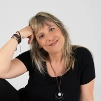 Smiling Mar Pavón in black top rests her head on her hand against a plain white background. childrnes spanish books.