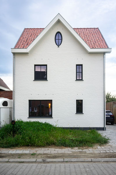 Ontdek de tijdloze elegantie van deze landelijke woning in Bornem, ontworpen door Pierrick Architect uit Temse. De voorgevel straalt een unieke charme uit met een wit gekaleide gevel die een perfect contrast vormt met de warme houten accenten en het stijlvolle zwarte buitenschrijnwerk. De klassieke uitstraling wordt versterkt door een eigenzinnige asymmetrische opdeling van de ramen, terwijl de achtergevel een overvloed aan natuurlijk licht biedt dankzij een grote raampartij in steel-look, compleet met dubbele deuren die uitkijken op de prachtige tuin.

Binnenin onthult de woning een hedendaagse indeling met een open plan, waarin elk aspect is ontworpen met de levensstijl van de bewoners in gedachten. De overdekte inkom, gelegen aan de zijgevel, verwelkomt gasten met een houten poort en dubbele deuren die toegang geven tot de fietsenberging. Elk detail getuigt van een persoonlijke aanpak, zorgvuldig afgestemd op de wensen van de bouwheer, wat resulteert in een woning die perfect aansluit bij de unieke levensstijl van de bewoners.

Deze schitterende creatie bevindt zich in Wintam, Bornem, en wordt gevangen in prachtige beelden vastgelegd door Rebecca Tanghe Fotografie. Ervaar de harmonie van traditionele allure en eigentijdse functionaliteit in de architectuur van Pierrick Architect.