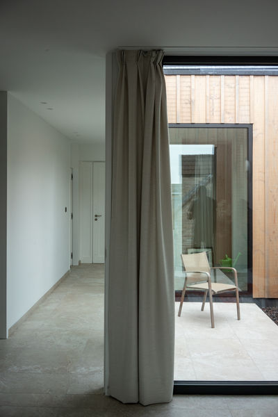 De patio van deze woning, ontworpen door Pierrick Architect, vormt het kloppende hart van de leefruimte. Een verborgen oase die rust en harmonie brengt in het dagelijkse leven. De doordachte vormgeving nodigt de natuur uit om de binnenruimte te omarmen, terwijl de architectuur en de natuurlijke elementen in perfecte harmonie samensmelten. De patio, als een levendig schilderij van licht en schaduw, creëert een serene plek waar de grenzen tussen binnen en buiten vervagen.