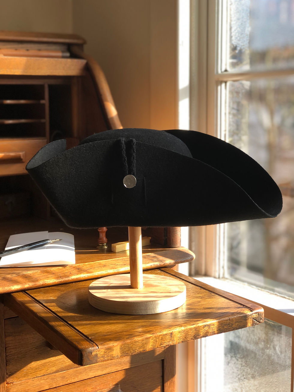 A black felt eighteenth century style cocked hat by a sash window on a wooden desk