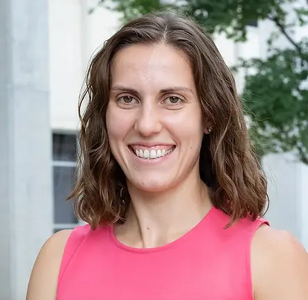 headshot: woman with wavy brown hair  wearing a pink top