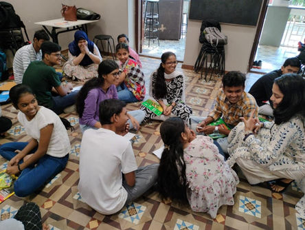 A group of teens and a facilitator seated on the floor in a circle during a creative, expressive arts-based group therapy session, smiling and engaging in open dialogue.
