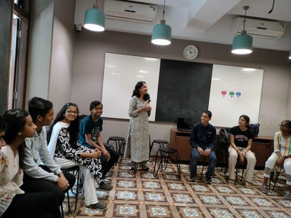 A facilitator leading a group of teenagers seated in a circle during a youth-focused session on communication and self-expression in a classroom setting.