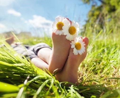Bild von 2 Füssen im Gras liegend, mit Margaritenblüten zwischen den Zehen