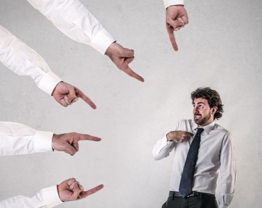 viele Finger, die tadelnd auf einen schuldbewussten Mann deuten