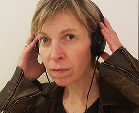 Photo of Alex Bulmer wearing a leather jacket and holding a pair of headphones to her ears