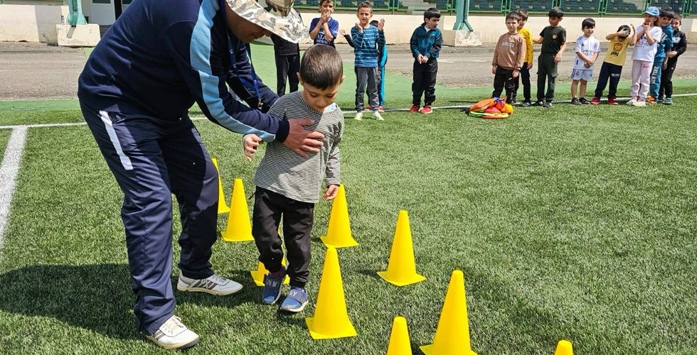 A coach helps a young player through soccer cones