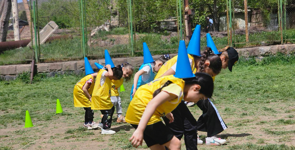 a group of kids balance soccer cones on their backs