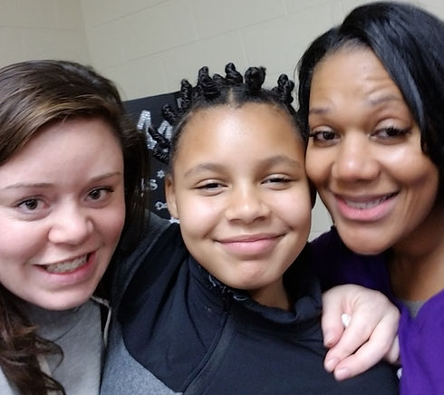 Two ladies of different colors and ages hugging a young girl.