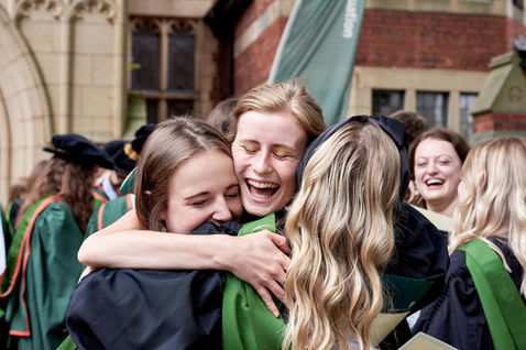 Three female students hugging in their graduation gowns