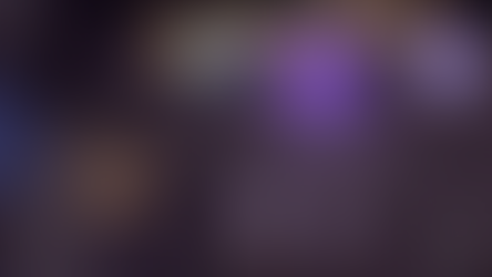 Um personagem de cabelo marrom e mochila azul nas costas observa um tubo de vidro cheio de água borbulhante. O personagem está em uma pequena vila, com duas casas pequenas ao seu lado. Objetos mecânicos brilhantes estão na parte de baixo da pequena vila. Ao lado do personagem existe uma energia rabiscada e roxa.