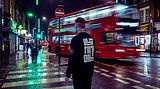 A tattooed model stands at a zebra crossing near Camden at night, back to the camera, wearing an oversized sweatshirt with the backprint in full view. Behind him, a red London bus speeds past in a blur, leaving a light trail