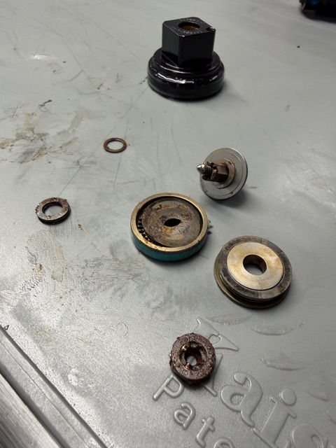 Disassembled rusty metal parts and washers on a gray workbench, with embossed text visible and a worn, mechanical workshop feel