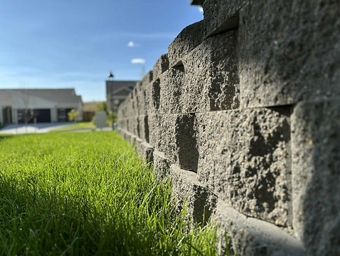 Stone retaining wall with fresh green lawn, installed for erosion control and landscape structure by Blue Bird Irrigation & Landscaping in Montana.
