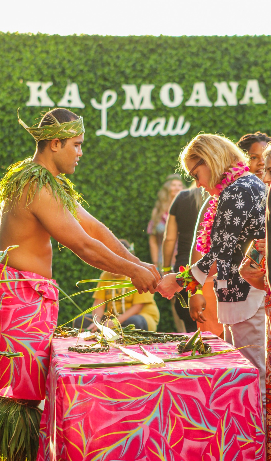 Guests making lei with a performer at the Ka Moana Luau sign