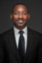 Erik Coleman smiling in a headshot, wearing a black suit, white shirt, black tie, against a neutral background
