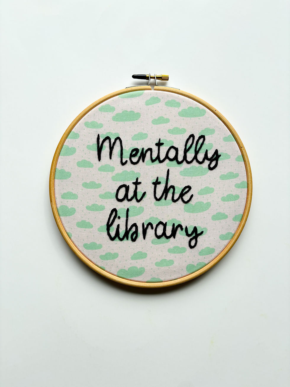 Thumbnail: Embroidery hoop with text: Mentally at the library, light green clouds background.