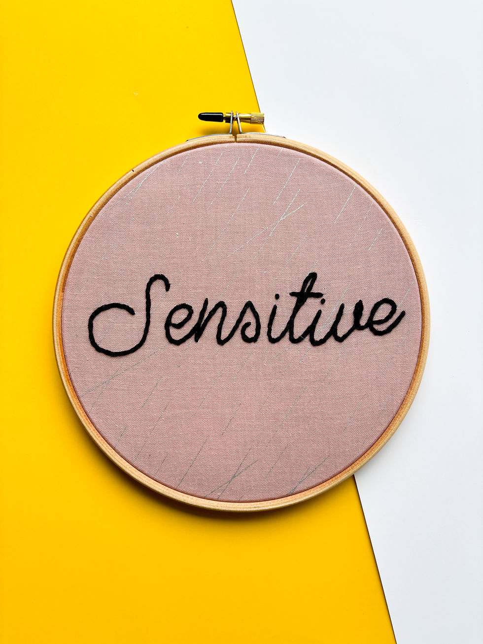 Embroidery hoop with the word "Sensitive" written in elegant script on soft cloth.