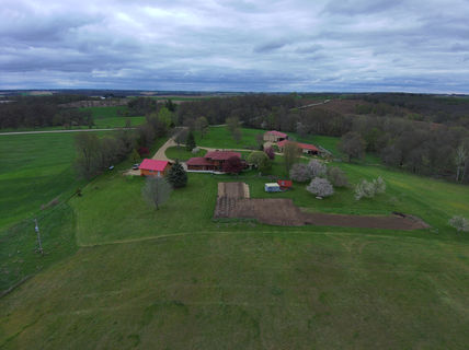 Aerial view of a farm house. Surrounded by green fields and trees.