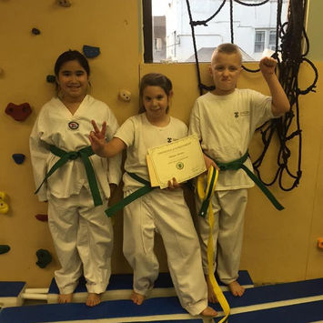 Three children with green belts, one holding a certificate