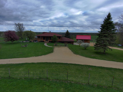 Large ranch house on green lawn and gravel driveway under cloudy sky.
