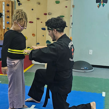 Instructor tying yellow belt on child in martial arts class
