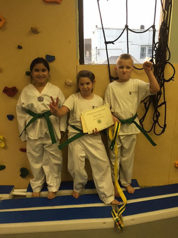 Three children with green belts, one holding a certificate